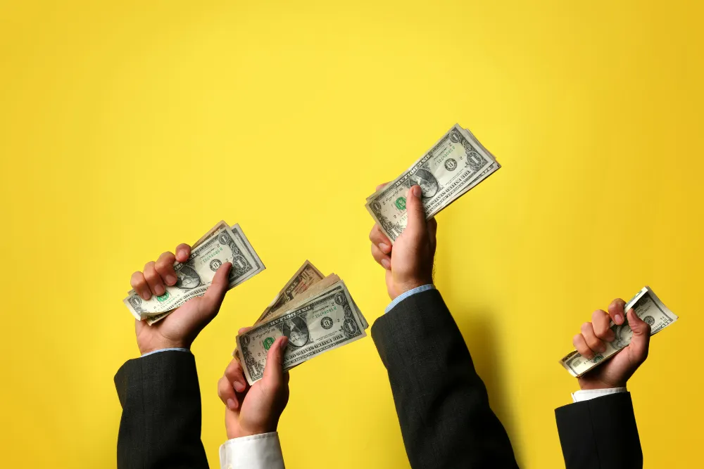 Business professionals displaying cash in their hands against a vibrant yellow background, symbolizing financial success.